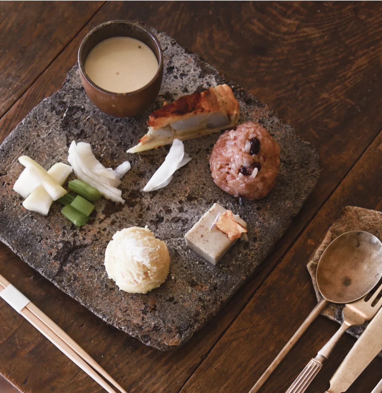 Artfully arranged meal on dark stone slab with rice, pickled vegetables, and ceramic cup