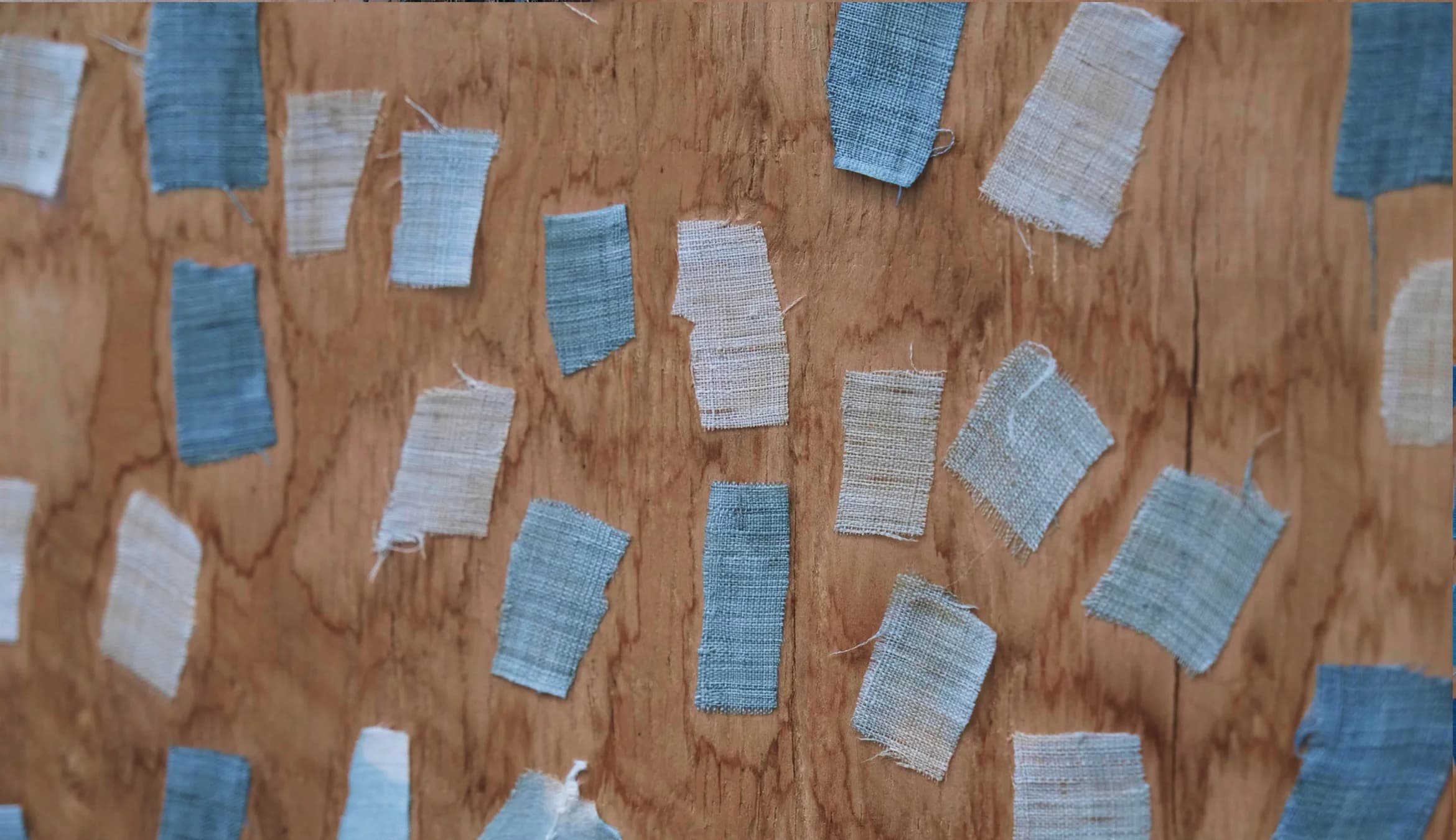 Hand pointing to a collection of textile samples on a plywood wall.