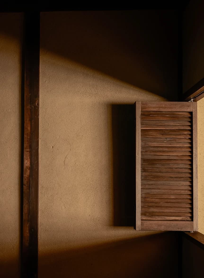 Wooden louvered window shutter against a clay plaster wall