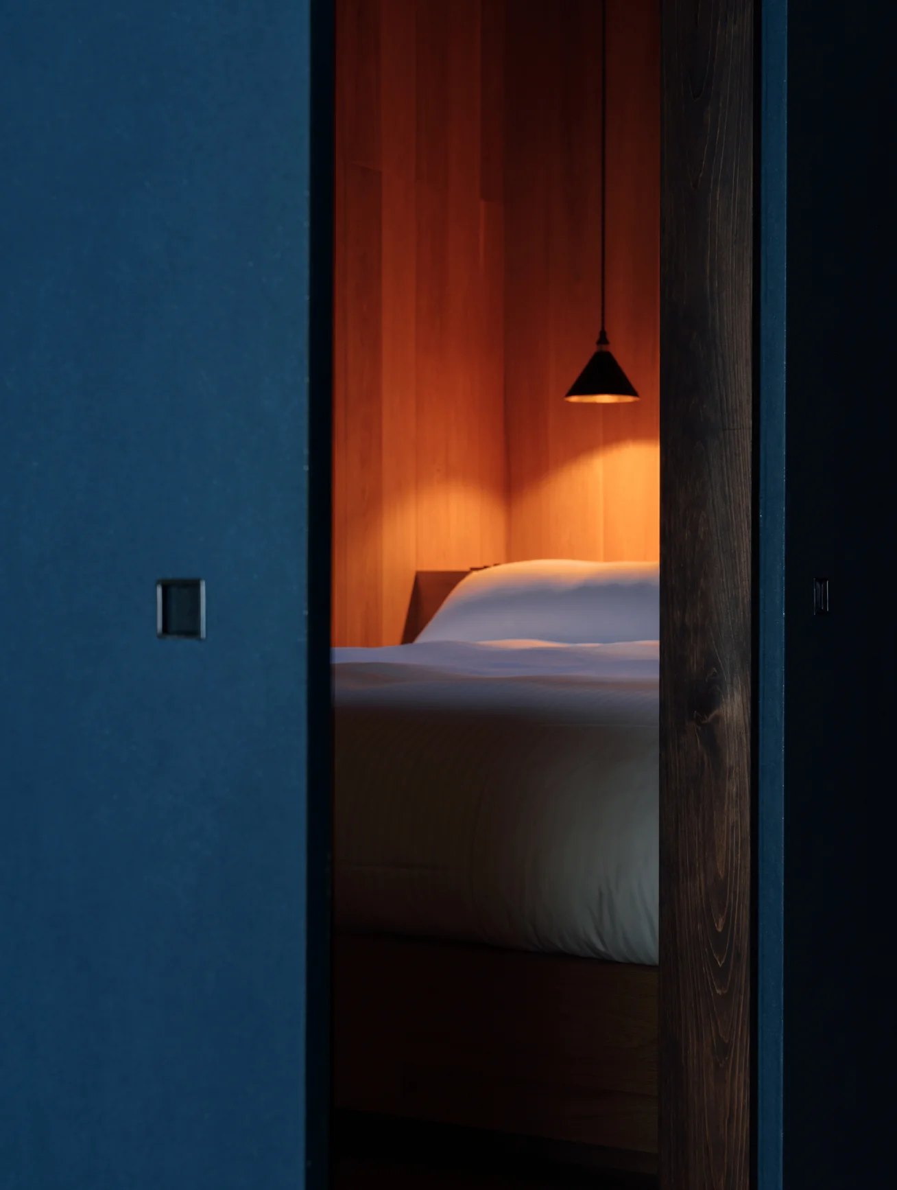 Bedroom glimpsed through a blue sliding door with pendant light