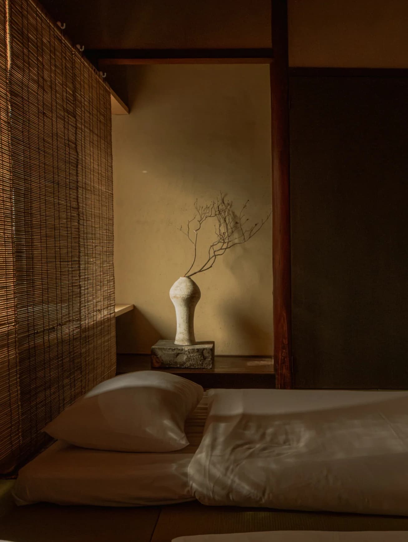 Futon bedding beside a tokonoma alcove with ceramic vase and branches