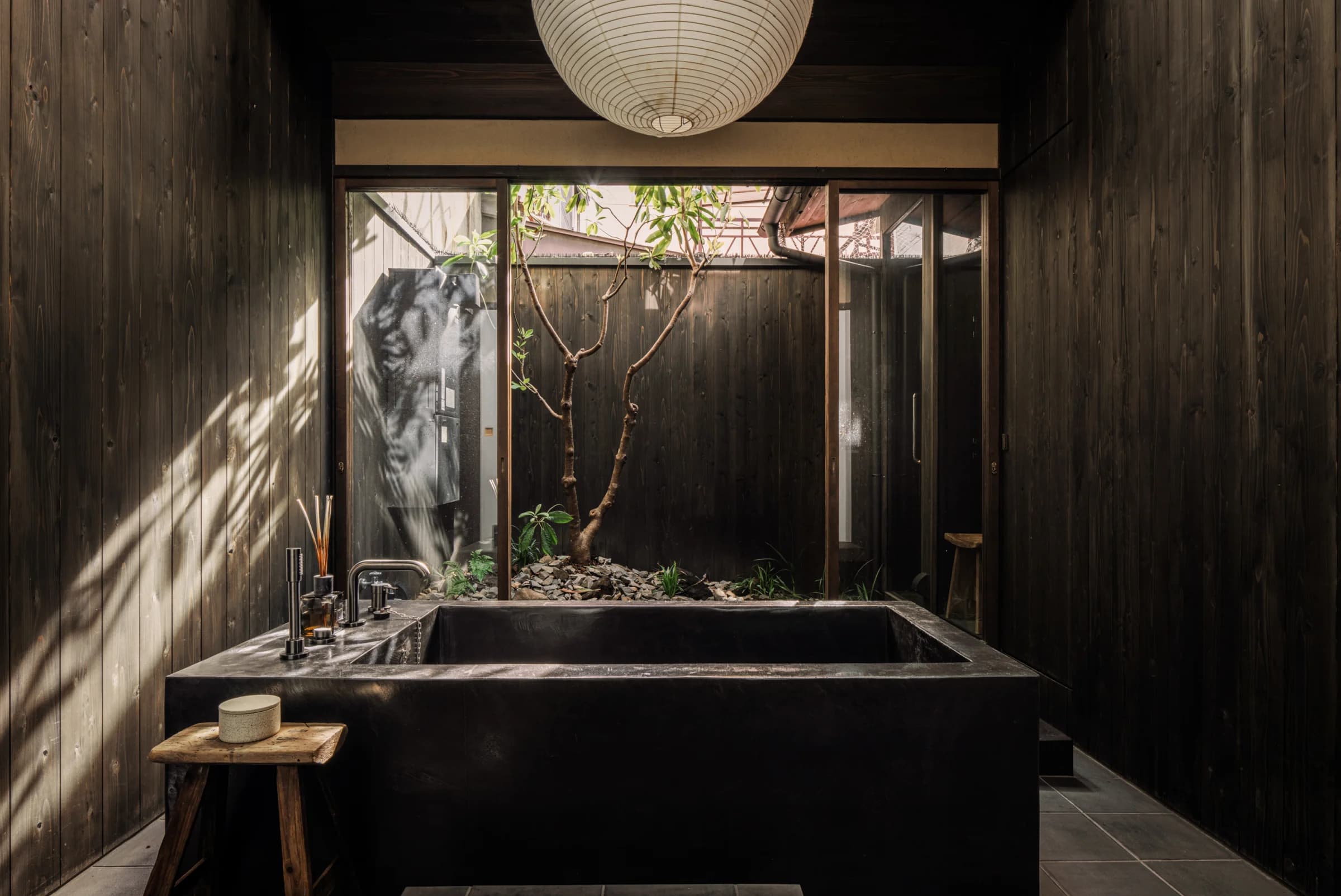 Paper lantern glowing in a wooden hallway with glass doors opening to a courtyard garden