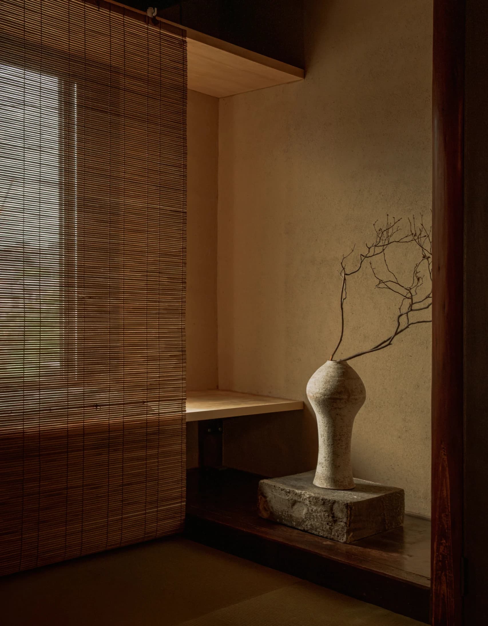 Ceramic vase on a wooden shelf beside a dark plastered wall with soft window light
