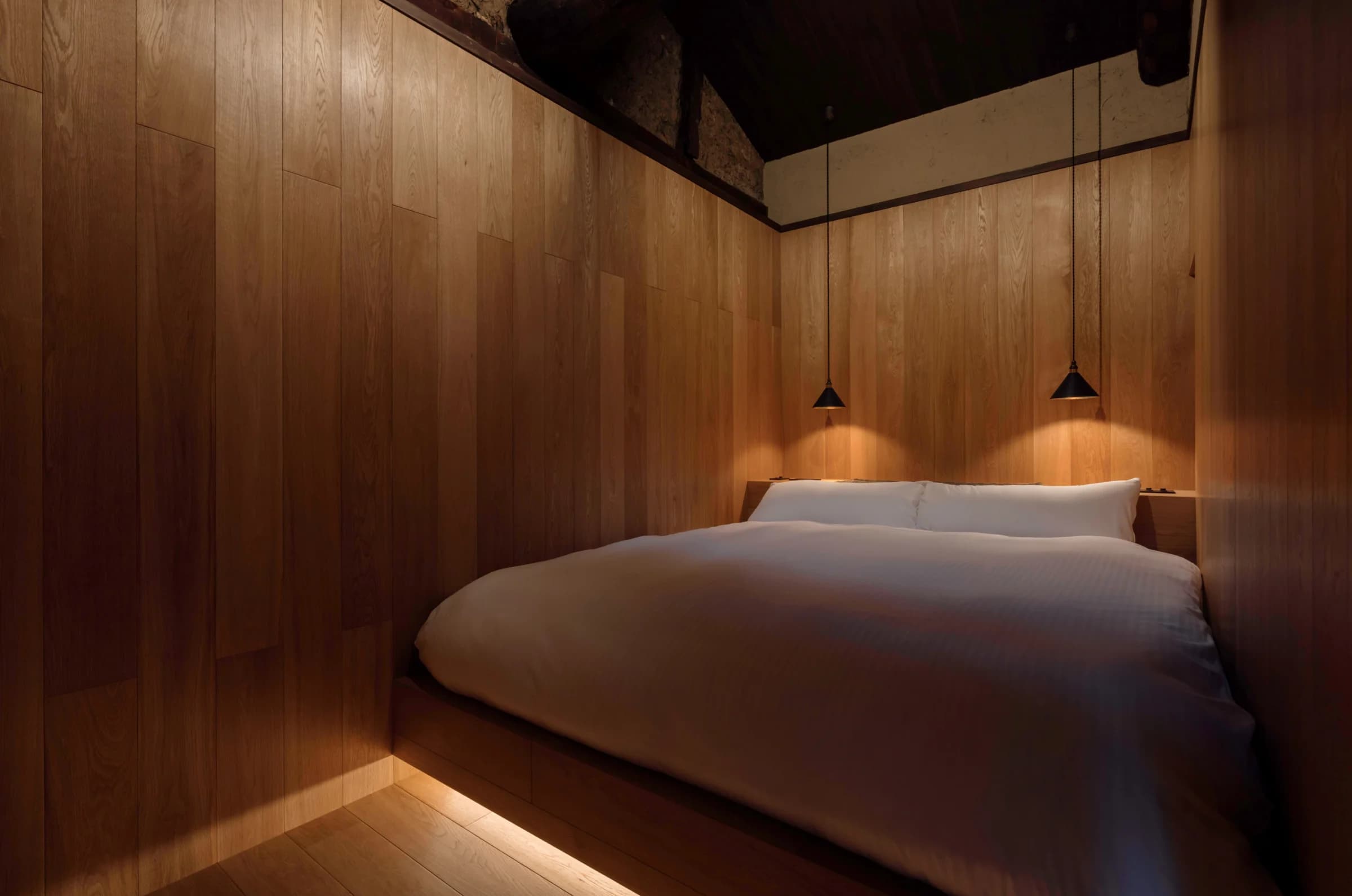 Platform bed with white linen in a wood-paneled bedroom with pendant light
